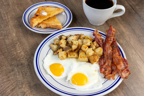 Breakfast plate with eggs, bacon, potatoes, toast, and a cup of coffee on a wooden table.
