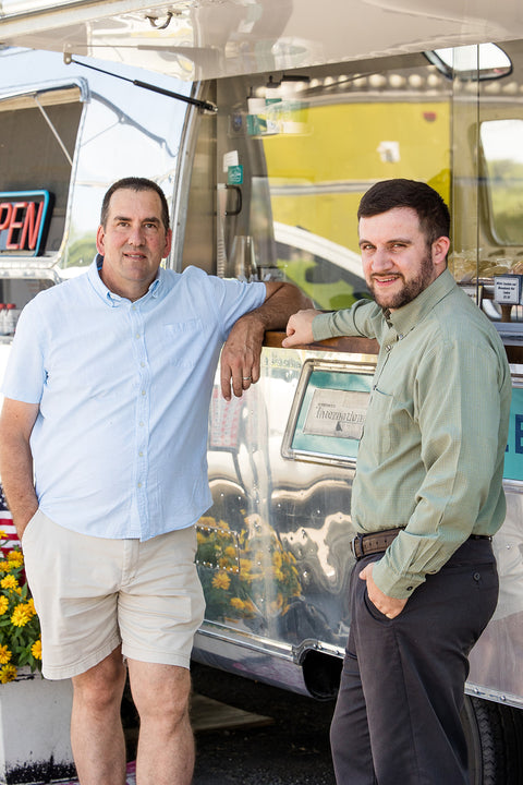 Two men standing next to a food truck with an open door