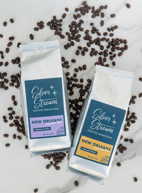 Two packages of Silver Stream Coffee Roasters New Orleans coffee on a marble surface with scattered coffee beans.